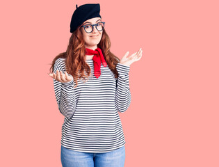 Young beautiful woman wearing french look with beret clueless and confused expression with arms and hands raised. doubt concept.