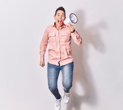 Young beautiful caucasian woman screaming using megaphone. Jumping over isolated white background