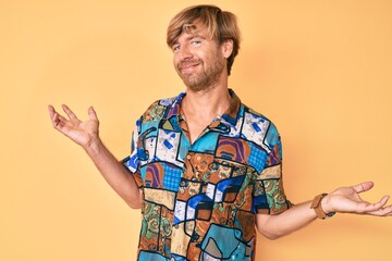 Young blond man wearing summer shirt clueless and confused expression with arms and hands raised....