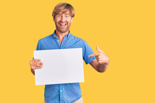 Handsome caucasian man with beard holding sale poster smiling happy pointing with hand and finger