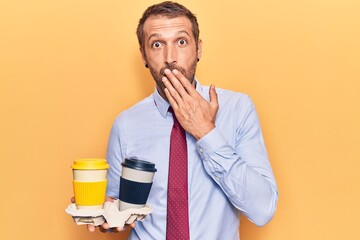 Young handsome man holding takeaway cup of coffee covering mouth with hand, shocked and afraid for mistake. surprised expression