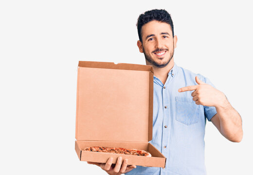 Young hispanic man holding delivery pizza box pointing finger to one self smiling happy and proud