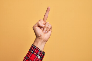 Hand of caucasian young man showing fingers over isolated yellow background showing provocative and rude gesture doing fuck you symbol with middle finger
