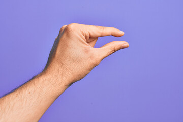 Hand of caucasian young man showing fingers over isolated purple background picking and taking invisible thing, holding object with fingers showing space