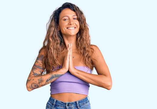 Young hispanic woman with tattoo wearing casual clothes praying with hands together asking for forgiveness smiling confident.