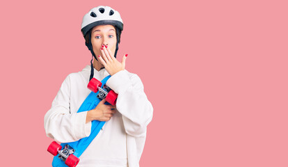 Beautiful brunette young woman wearing safety helmet and skate covering mouth with hand, shocked and afraid for mistake. surprised expression