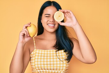Young beautiful asian girl holding lemon winking looking at the camera with sexy expression,...
