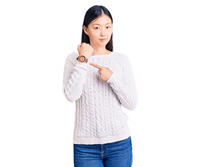 Young beautiful chinese woman wearing casual sweater in hurry pointing to watch time, impatience, looking at the camera with relaxed expression