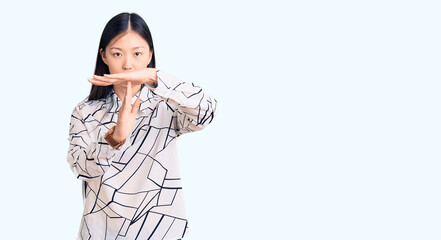 Young beautiful chinese woman wearing casual shirt doing time out gesture with hands, frustrated...