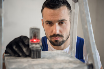 The man in gloves and work clothes makes the markings with the help of the leveling tool