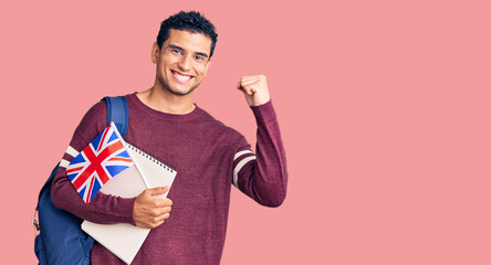 Hispanic handsome young man exchange student holding uk flag screaming proud, celebrating victory and success very excited with raised arms