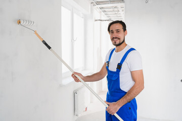 Medium shot, workman in blue work clothes paints wall in apartment