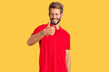 Handsome blond man with beard wearing casual clothes doing happy thumbs up gesture with hand. approving expression looking at the camera showing success.