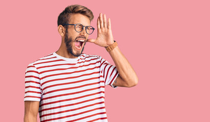 Handsome blond man with beard wearing casual clothes and glasses shouting and screaming loud to side with hand on mouth. communication concept.