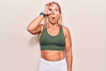 Middle age caucasian blonde woman wearing sportswear doing ok gesture shocked with surprised face, eye looking through fingers. unbelieving expression.