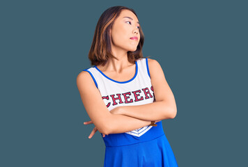 Young beautiful chinese girl wearing cheerleader uniform looking to the side with arms crossed...