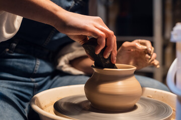 a Potter girl sculpts a pot on a Potter's wheel with her hands and tools