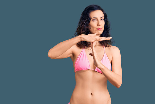 Young beautiful hispanic woman wearing bikini doing time out gesture with hands, frustrated and serious face