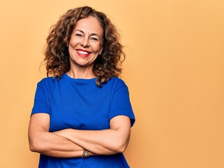 Middle age beautiful woman wearing casual t-shirt standing over isolated yellow background happy face smiling with crossed arms looking at the camera. Positive person.