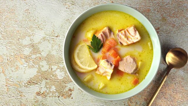 Top view of plate with delicious creamy salmon chowder soup and golden spoon on pastel green background. Rotation from right to left. 4K UHD