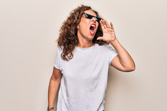Middle age beautiful woman wearing funny thug life sunglasses over white background shouting and screaming loud to side with hand on mouth. Communication concept.