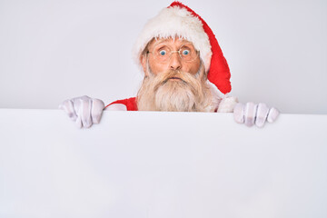 Naklejka premium Old senior man with grey hair and long beard wearing santa claus costume holding banner puffing cheeks with funny face. mouth inflated with air, catching air.