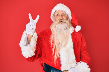 Old senior man with grey hair and long beard wearing traditional santa claus costume showing and pointing up with fingers number two while smiling confident and happy.