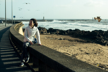 Asian woman sits on the waterfront during the surf and gulls around.