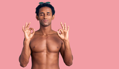 African handsome man wearing swimsuit and sunglasses relax and smiling with eyes closed doing meditation gesture with fingers. yoga concept.