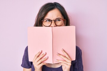 Young beautiful woman wearing glasses reading book angry and mad screaming frustrated and furious, shouting with anger. rage and aggressive concept.