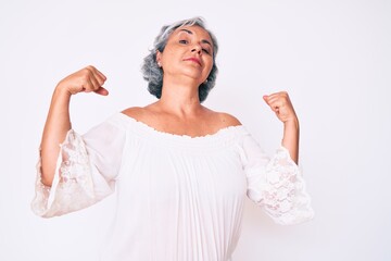 Senior hispanic grey- haired woman wearing casual clothes showing arms muscles smiling proud. fitness concept.