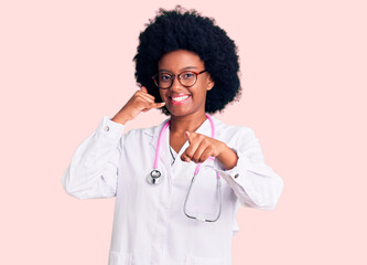 Young african american woman wearing doctor coat and stethoscope smiling doing talking on the telephone gesture and pointing to you. call me.