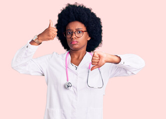 Young african american woman wearing doctor coat and stethoscope doing thumbs up and down, disagreement and agreement expression. crazy conflict