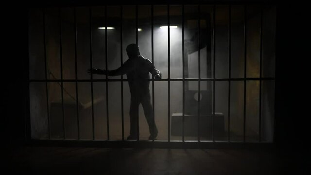 Execution concept. Death penalty guillotine miniature inside old prison. Old prison bars cell lock. Man inside jail. Horror view of Guillotine scale model in the dark