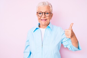 Senior beautiful woman with blue eyes and grey hair wearing glasses smiling happy and positive, thumb up doing excellent and approval sign