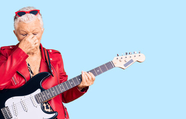 Senior beautiful woman with blue eyes and grey hair wearing a modern look playing electric guitar tired rubbing nose and eyes feeling fatigue and headache. stress and frustration concept.