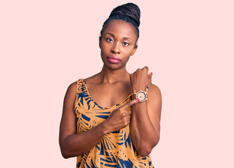 Young african american woman wearing casual clothes in hurry pointing to watch time, impatience,...