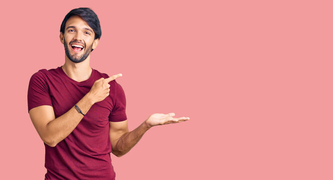 Handsome hispanic man wearing casual clothes amazed and smiling to the camera while presenting with hand and pointing with finger.