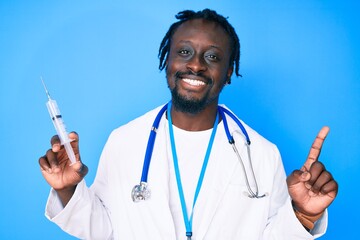 Young african american man with braids wearing doctor stethoscope holding syringe surprised with an...