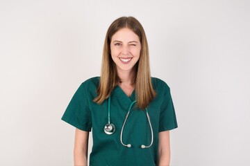 Coquettish Female doctor wearing a green scrubs and stethoscope, smiling happily, blinking at...