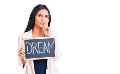 Young beautiful latin girl holding blackboard with dream word serious face thinking about question...