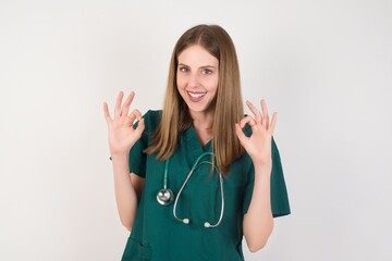 Female doctor wearing a green scrubs and stethoscope showing both hands with fingers in OK sign....