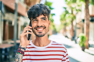 Young hispanic man smiling happy and talking on the smartphone at street of city