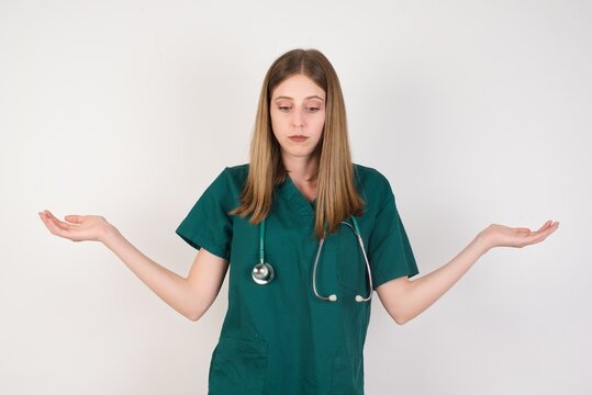 Hesitant  Female Doctor Wearing A Green Scrubs And Stethoscope Shrugs Shoulders, Looks Uncertain And Confused. Have No Answer