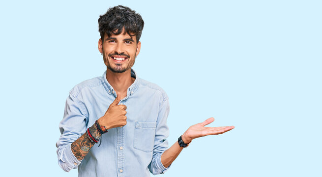 Young hispanic man wearing casual clothes showing palm hand and doing ok gesture with thumbs up, smiling happy and cheerful