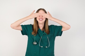 Female doctor wearing a green scrubs and stethoscope covering eyes with hands smiling cheerful and funny. Blind concept.