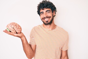 Handsome young man with curly hair and bear holding brain as mental health concept looking positive...