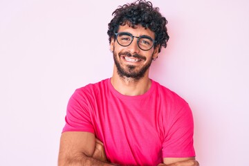 Handsome young man with curly hair and bear wearing casual clothes and glasses happy face smiling...