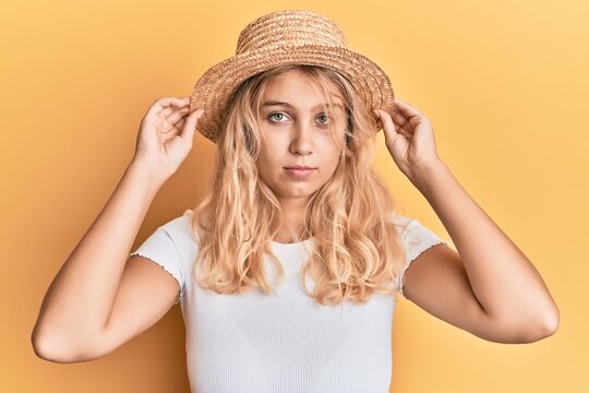 Young blonde girl wearing summer hat relaxed with serious expression on face. simple and natural looking at the camera.