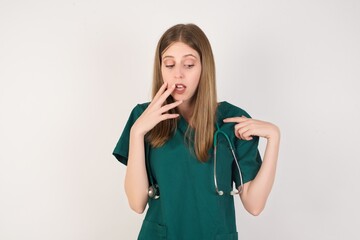 Shocked Female doctor wearing a green scrubs and stethoscope look surprisedly down, indicates at blank  with fore finger, . Scared male finds out price on usual shirt from luxury shop